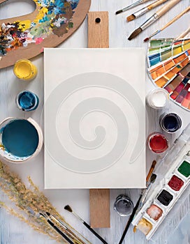 A white canvas with a wooden board and a variety of paint colors and brushes