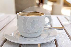 White cappuccino cup on a white wooden table on a sunny summer