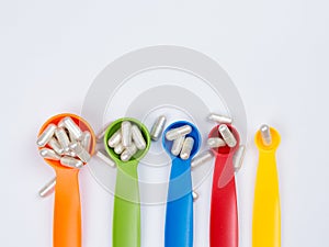 White capsules pills spilling out of the colorful measuring spoon on white background.