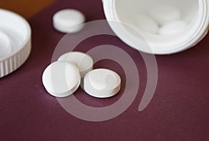 white capsules poured out of the container, red, burgundy background, close-up