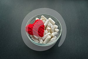 White capsules, tablets in round plate with red thread heart on