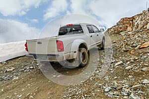 White car with a body rides up a stony road to the top of a rock
