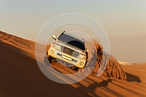 White car driving in Rub al Khali Desert at the Empty Quarter, in Abu Dhabi, United Arab Emirates at sunset