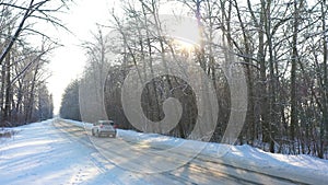 White car fast riding through snow covered icy road. SUV going at empty countryside route in winter forest on sunny day