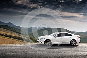 White car parked at countryside asphalt road near green mountains