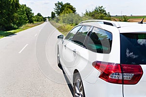 A white car is parked on a sunny road, ready for a journey amidst greenery and clear skies. The scene exudes tranquility