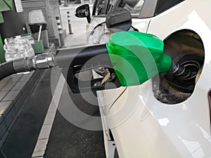 White car refueling at gas station with green fuel nozzle
