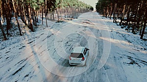 White car rides along winter country road between trees in forest with snow