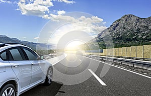 A white car rushing along a high-speed highway in the sun.