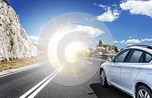 A white car rushing along a high-speed highway in the sun.