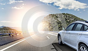 A white car rushing along a high-speed highway in the sun.