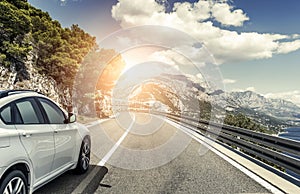 A white car rushing along a high-speed highway in the sun.