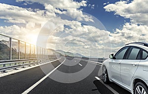 A white car rushing along a high-speed highway in the sun.