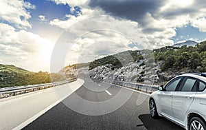 A white car rushing along a high-speed highway in the sun.