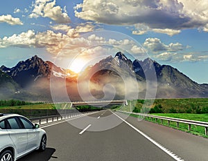 A white car rushing along a high-speed highway in the sun.