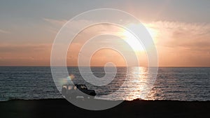 White car standing on cliff against pink sunset. Cliff with car standing on it and amazing view of ocean. Vehicle standing near e