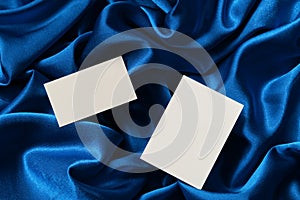 White card on a chic blue satin background, top view