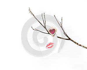 White card with lip print hanging on a bare winter tree branch pinned with a clothespin with a red heart for Valentine`s Day.