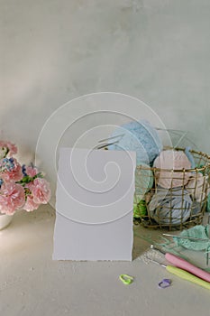 White card Mockup on light background, knitting threads in pastel colors, metal knitting needles