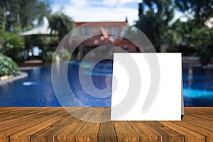 White card put on wood table and beautiful view of swiming pool at resort in background. product display template.