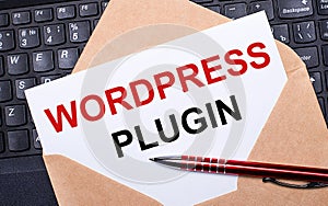 White card with the text WORDPRESS PLUGIN in a craft envelope on a work desk with a modern laptop keyboard and burgundy pen. Flat