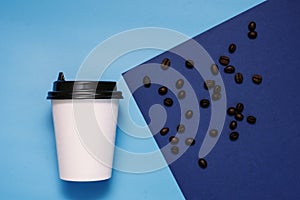 White cardboard glass with a plastic black lid on a blue and cyan background with coffee beans. Glass with take-away