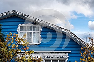 White carved platbands on the windows and the ridge of the roof of a blue house