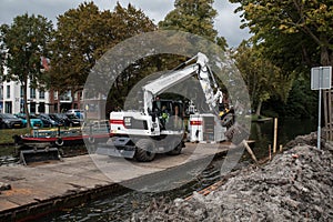 White Cat industrial digger floating on a raft barge on a river canal and excavating the bank