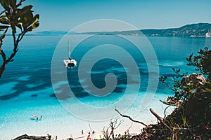 White catamaran yacht at anchor on clear azure water surface in calm blue lagoon. Unrecognizable tourists leisure on the