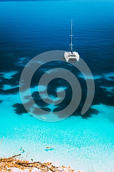 White catamaran yacht drift on clear azure water surface in calm blue lagoon with transparent water and dark pattern on