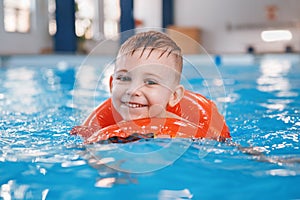White Caucasian child in swimming pool. Preschool boy training to float with red circle ring in water