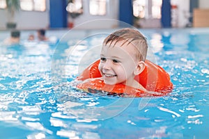 White Caucasian child in swimming pool. Preschool boy training to float with red circle ring in water