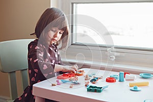 White Caucasian preschooler girl playing plasticine playdough indoors at home