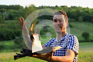 White Caucasian young man or adult guy reading a burning book on blurred forest background. Emotion of expression