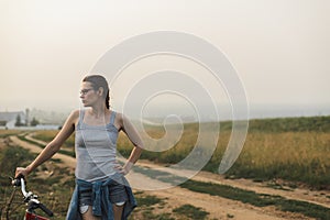 White caucasian young woman standing with bike on hill near road