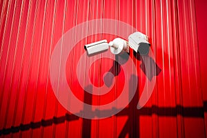 A white CCTV camera mounted next to a red metal wall for the background. Installing CCTV cameras in public areas to record footage