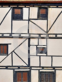 White cement rough wall facade background with black wooden slats and old small windows. Detail of beams, lumber and other