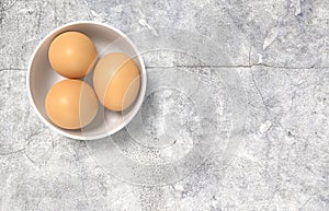 White ceramic bowl ful of eggs. Placed on concrete table.