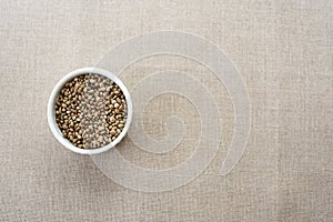 A white ceramic bowl full of hemp seeds over linen background