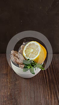 White ceramic bowl with natural healthy flavours for herbal tea and hot dinks half of lemon, fresh mint and ginger on