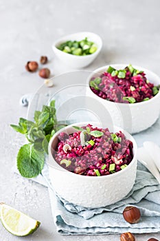 White ceramic bowls with buckwheat, beetroot, nuts and herbs warm salad, light grey concrete background.