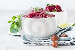 White ceramic bowls with buckwheat, beetroot, nuts and herbs warm salad, light grey concrete background.