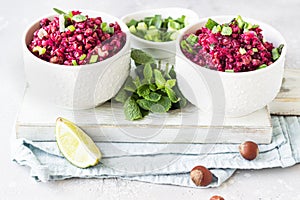 White ceramic bowls with warm buckwheat, beetroot, nuts and herbs salad on wooden board, light grey concrete background.