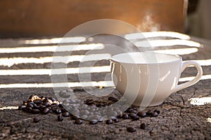 White ceramic coffee cup on a rustic wooden table with coffee beans under the morning sunshine through the fence