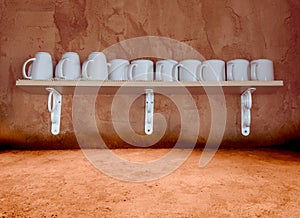 White ceramic coffee cup on the wooden shelf with grunge cement background,retro filter effect