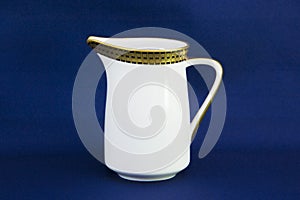 White ceramic creamer on a saucer with cold cream on a blue background.