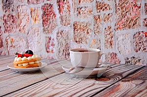 White ceramic cup of black tea with a spoon on a saucer and a plate with a biscuit cake with cream, cherry and strawberries