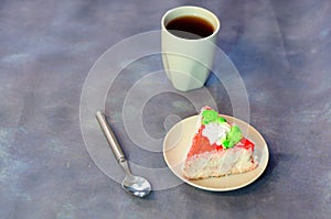 White ceramic cup of coffee, a spoon and a tarekla with a triangular piece of cake in red icing