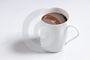 White ceramic cup of hot cocoa on top of white marble background