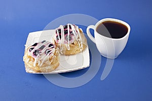 White ceramic cup of hot coffee and sweet pastries on blue background